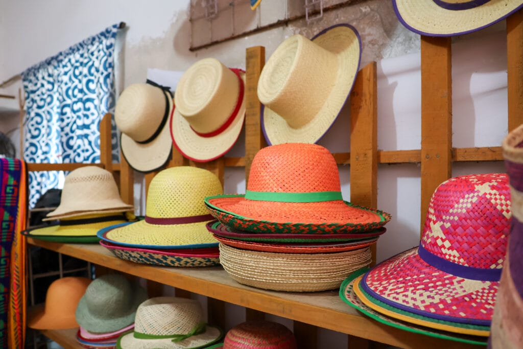 Ein Holzgestell mit Strohhüten in verschiedenen Farben.